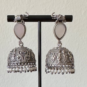 May include: A pair of silver dangle earrings with a white stone and pearl accents. The earrings feature an intricate design with an elephant at the top.