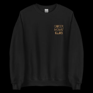 Pode incluir: Camisola preta com o texto "QUEER MOMS' CLUB" em letras douradas no peito. A camisola é de cor preta lisa e parece ser feita de um material macio.