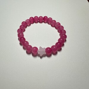 Op de afbeelding: Een roze kralen armband met een witte ster bedel.
