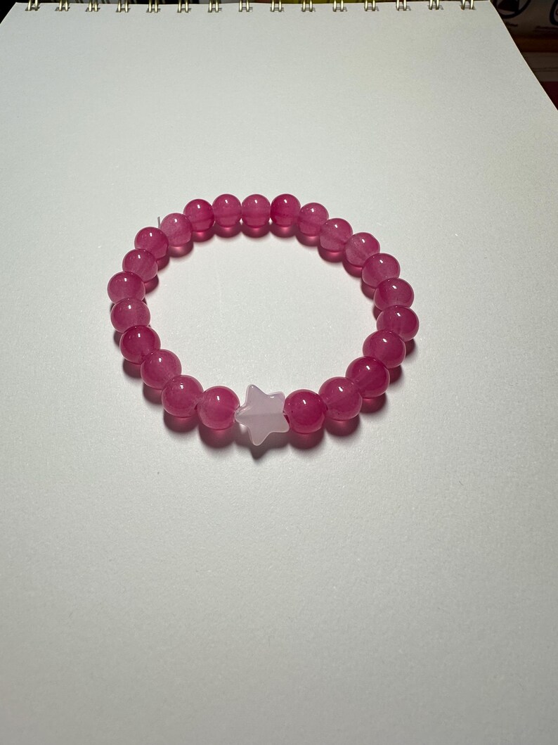 Op de afbeelding: Een roze kralen armband met een witte ster bedel.