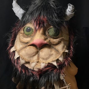 Op de afbeelding: Een handgemaakt monstermasker met zwart bont, rode accenten en groene ogen. Het masker is gemaakt van jute en heeft een genaaide neus en mond.