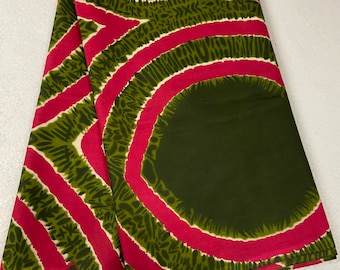 May include: A folded fabric with a green and pink pattern. The pattern features large circles with a green center and pink outlines. The circles are surrounded by smaller green and white patterns.