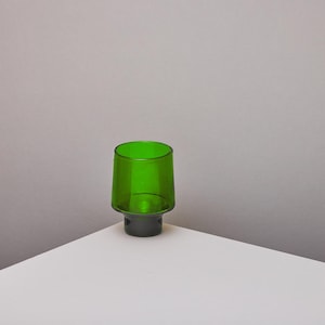 Op de afbeelding: Een groene glazen tumbler met een donkergroene basis. De tumbler staat op een wit oppervlak.