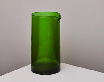 May include: A tall, green glass pitcher with a wide mouth and a slightly curved lip.