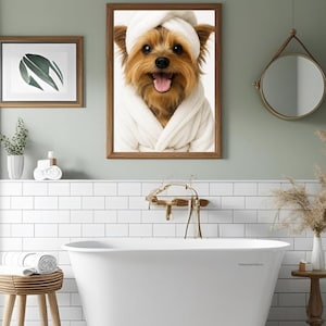 May include: A bathroom scene featuring a framed picture of a dog wearing a white robe and towel. The room has a white bathtub, a round mirror, and a wooden stool. The walls are painted a light green color.