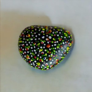 May include: A heart-shaped rock painted black with white, green, yellow, red, and blue polka dots.