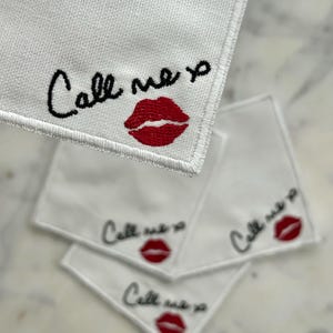 K&ouml;nnte beinhalten: Wei&szlig;e quadratische Taschent&uuml;cher mit gesticktem Text "Call me xo" in schwarzer Schrift und einem roten Lippenabdruck. Die Taschent&uuml;cher sind aus einem strukturierten Stoff.