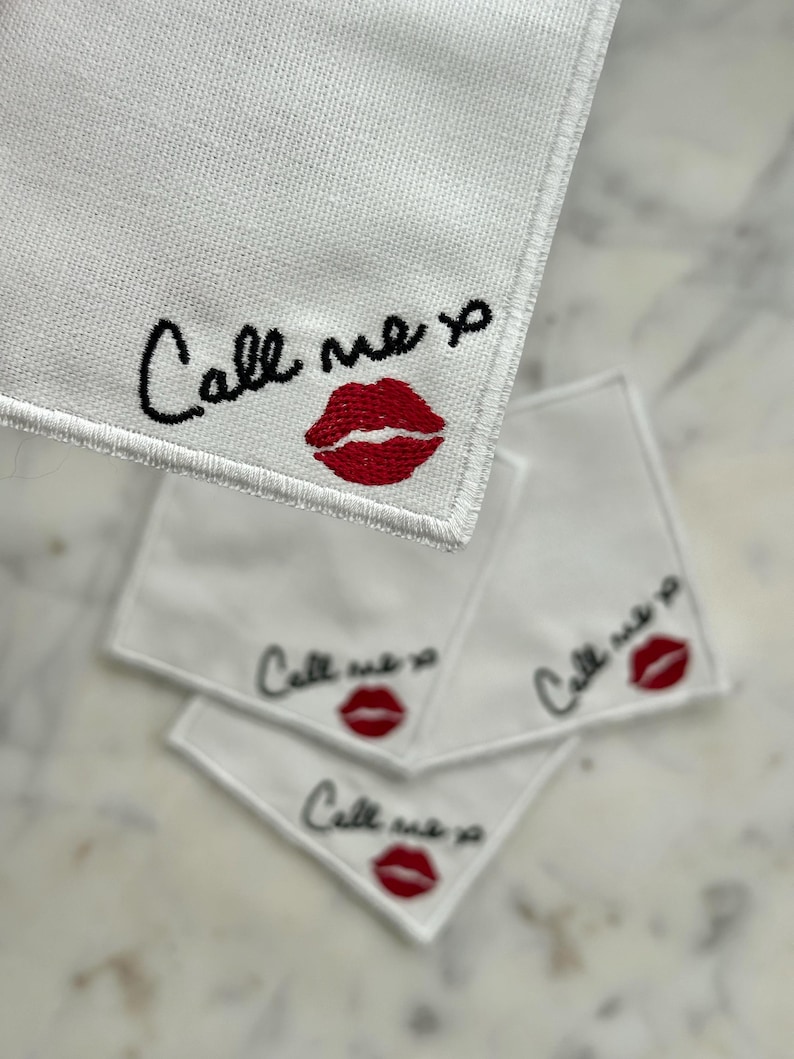 K&ouml;nnte beinhalten: Wei&szlig;e quadratische Taschent&uuml;cher mit gesticktem Text "Call me xo" in schwarzer Schrift und einem roten Lippenabdruck. Die Taschent&uuml;cher sind aus einem strukturierten Stoff.