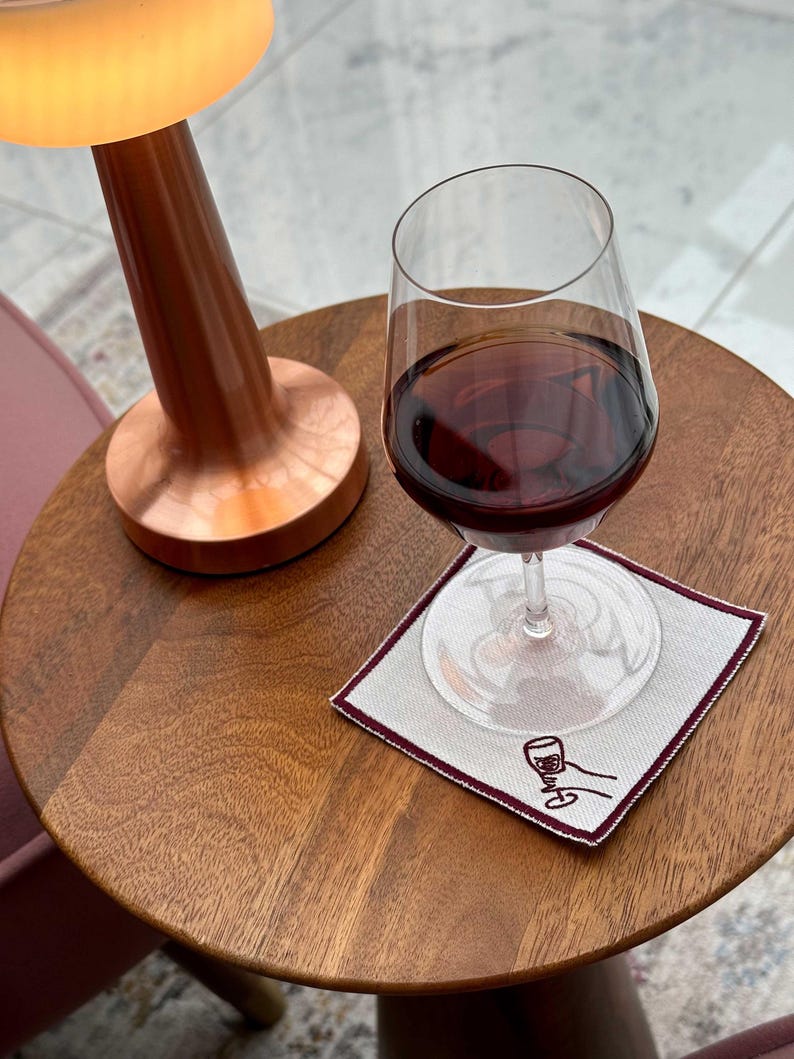 A glass of wine on a cotton coaster with an embroidered hand holding a wine glass in a raised cheers position