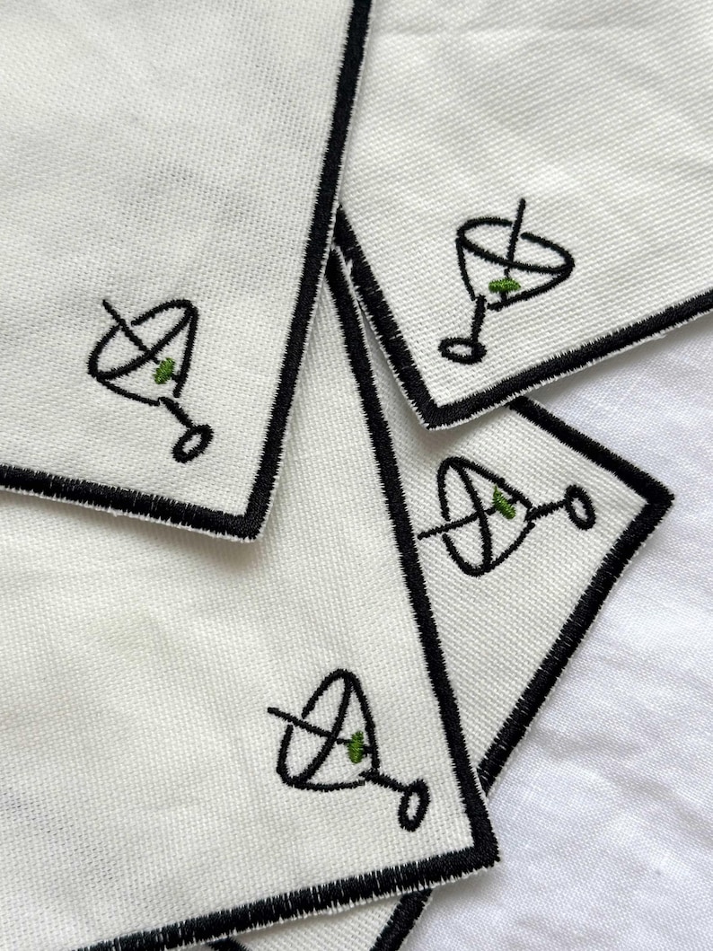 Four embroidered white cotton cocktail coasters with black stitching of a martini glass