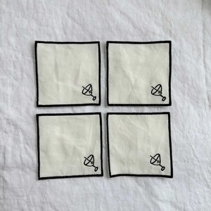 Four embroidered white cotton cocktail coasters with black stitching of a martini glass
