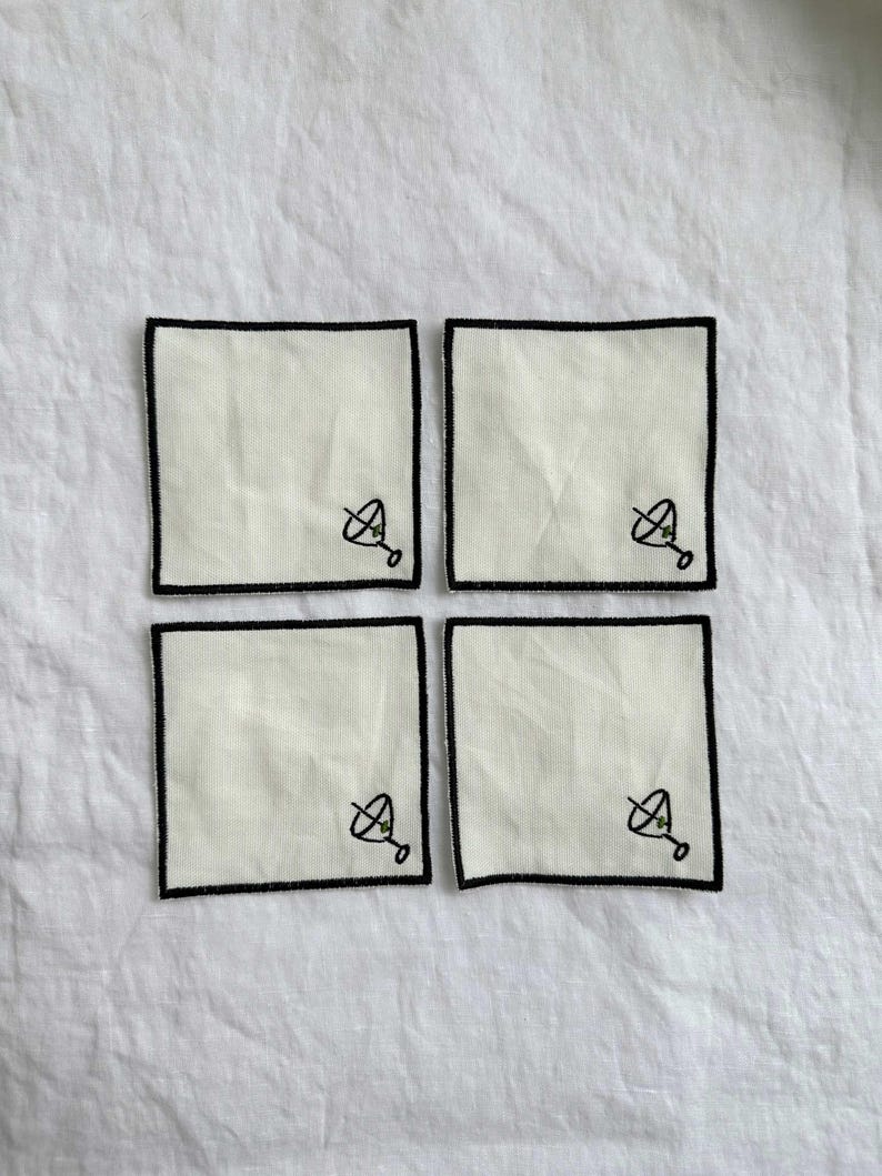 Four embroidered white cotton cocktail coasters with black stitching of a martini glass