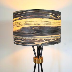 Puede incluir: Una lámpara de pie de madera con vetas negras y amarillas, con una base dorada y tres patas negras.