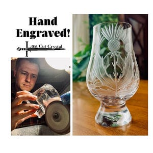May include: Hand-engraved crystal glass with a thistle design. The clear glass features detailed etched artwork of a thistle plant. The glass has a rounded bowl shape and a sturdy base. The text "Hand Engraved! Last Cut Crystal" is visible.