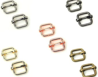 Op de afbeelding: Set van 10 metalen schuifgespen in vijf verschillende afwerkingen: zilver, zwart, rosé goud, goud en antiek messing. Elke gesp is vierkant met een afgeronde rand en een centrale lus.