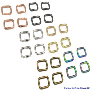 May include: Assortment of metal D-rings in various finishes, including silver, gold, brass, black, and rainbow. The D-rings are arranged in rows on a white background.  EMMALINE HARDWARE is printed at the bottom of the image.