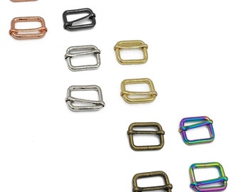 Op de afbeelding: Assortiment van 10 metalen schuifgespen in verschillende afwerkingen, waaronder zilver, goud, zwart, brons en regenboog. De gespen zijn allemaal dezelfde maat en vorm, met een rechthoekig ontwerp en een kleine opening aan één kant.