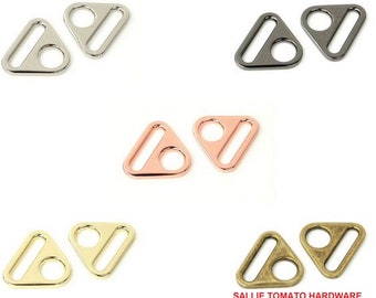 Puede incluir: Cinco pares de anillos metálicos en forma de triángulo en diferentes acabados: plata, negro, oro rosa, oro y latón antiguo. Cada anillo tiene una abertura rectangular en el centro.
