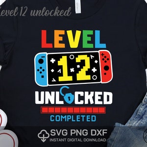 May include: A black t-shirt with a colorful graphic of a video game controller and the text "Level 12 Unlocked" and "Completed".