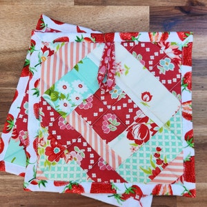 May include: Two red and white quilted pot holders with a strawberry print. The pot holders have a diamond pattern and a fabric loop for hanging.