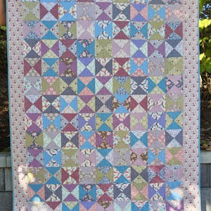 May include: A patchwork quilt with a variety of floral patterns in shades of pink, purple, blue, and green. The quilt is made up of small squares and triangles, and it has a blue border.