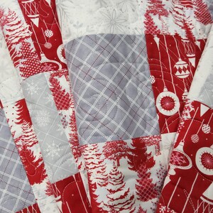 May include: A patchwork quilt with a festive Christmas theme. The quilt features red, white, and gray squares with patterns of Christmas trees, ornaments, and snowflakes. The quilt is machine-stitched with a quilted design.