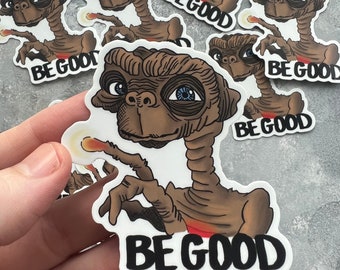 May include: A collection of stickers featuring the character E.T. with the text "BE GOOD". The stickers depict E.T. with brown skin, large blue eyes, and a glowing finger. The stickers are on a white background.