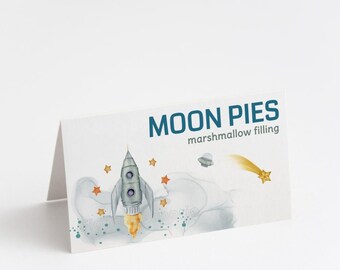 May include: A white card with blue text that reads "MOON PIES marshmallow filling". The card features a watercolor illustration of a rocket ship flying through space with stars and a comet.