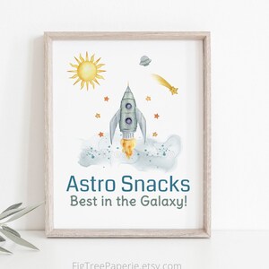 May include: A watercolor illustration of a rocket ship flying through space with a yellow sun, a comet, and stars. The text "Astro Snacks Best in the Galaxy!" is below the rocket ship.