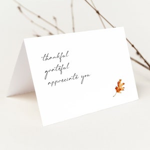 May include: A white card with the words "thankful grateful appreciate you" written in black cursive. A small brown leaf is in the bottom right corner.
