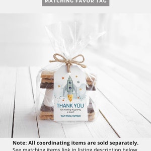 K&ouml;nnte beinhalten: Ein klarer Zellophanbeutel, der mit Bindfaden gebunden ist und Kekse und ein Geschenk-Etikett enth&auml;lt. Das Etikett zeigt ein Aquarell-Raketendesign mit dem Text "THANK YOU" und personalisiertem Text. Der Text "MATCHING FAVOR TAG" steht oben.