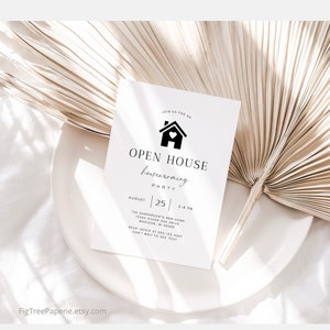 May include: A white card with black text announcing an open house housewarming party on August 25th from 5-8 PM. The address is 12345 Silver Oak Drive, Madison, WI 00000. The RSVP number is 000-123-4567. The card features a black silhouette of a house with a heart in the window.