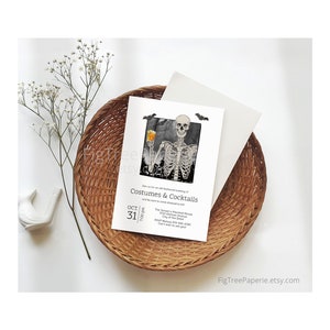 May include: Halloween-themed invitation with a skeleton holding a drink, set against a black and white background. The invitation is on a white card, with the text "Costumes & Cocktails" and event details. The card is placed in a woven basket.