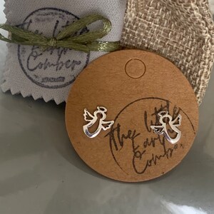 May include: Two silver angel earrings on a brown card with the text "The Little Earthen Comber".