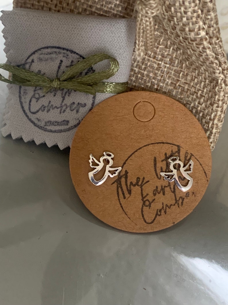 May include: Two silver angel earrings on a brown card with the text "The Little Earthen Comber".