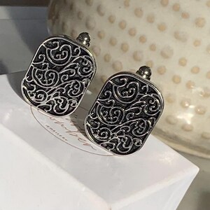 May include: A pair of silver cufflinks with a black, intricate, floral design.