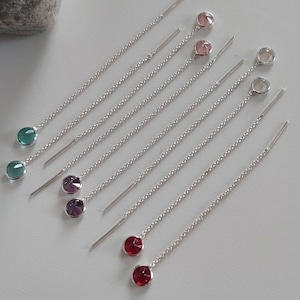 May include: A collection of delicate silver threader earrings. Each earring features a small, round gemstone in various colors, including teal, purple, pink, and red. The gemstones are set at the end of a long, thin chain.