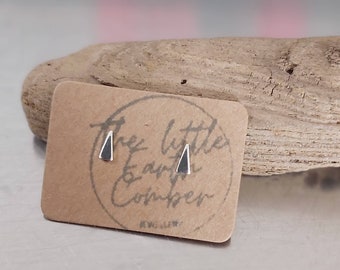 May include: A pair of small silver triangle stud earrings on a brown card with the text "The Little Earth & Co.mber" in black lettering.