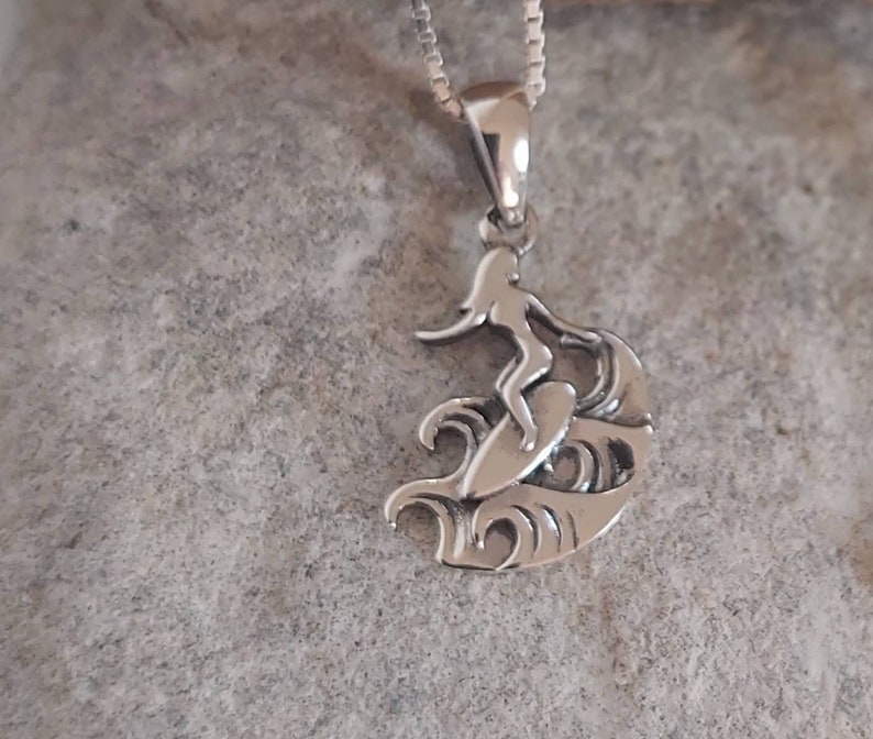 Puede incluir: Colgante de plata con dise&ntilde;o de surfista. El colgante muestra un surfista sobre una tabla, surfeando una ola. La cadena es fina y el acabado pulido. Un accesorio cl&aacute;sico con tem&aacute;tica de surf.
