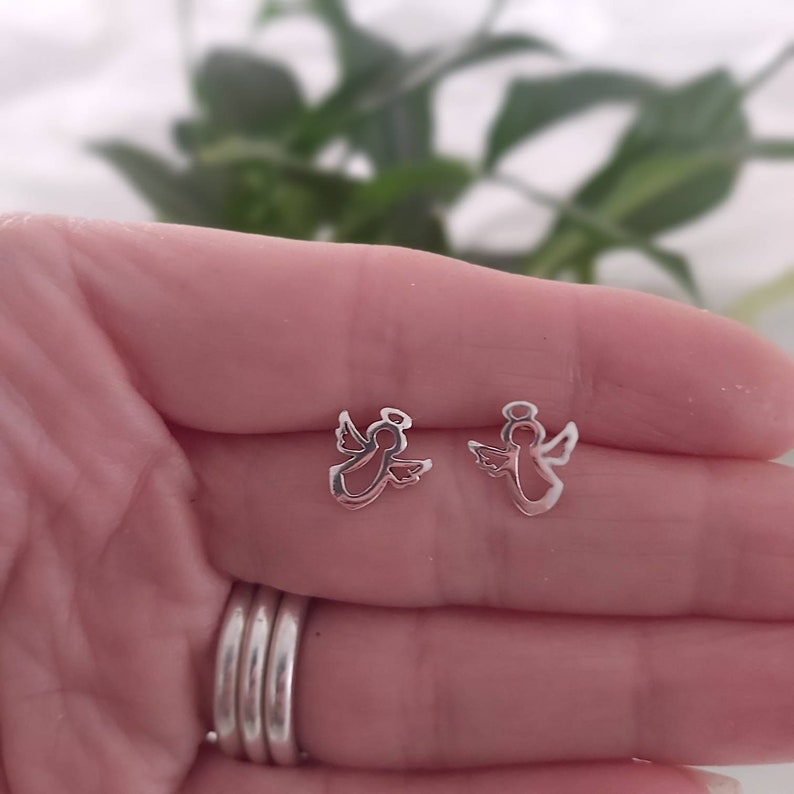 May include: A pair of silver angel stud earrings. The earrings are small and delicate, and they feature a simple design of an angel with wings outstretched.