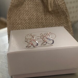 May include: A pair of silver angel wing earrings in a white box with the text "The Little and Home" on the lid.