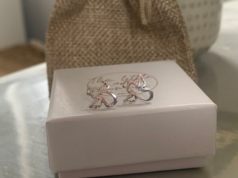 May include: A pair of silver angel wing earrings in a white box with the text "The Little and Home" on the lid.