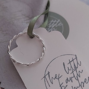 May include: A silver twisted band ring on a white card with the text "The Little Earth Dreamer" in black script.