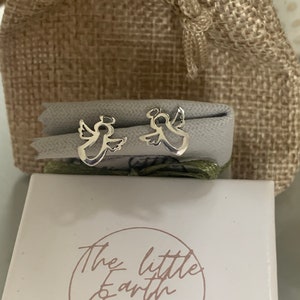 May include: A pair of silver angel earrings in a small white box with the text "The Little Earth Comber Jewellery" on the front.