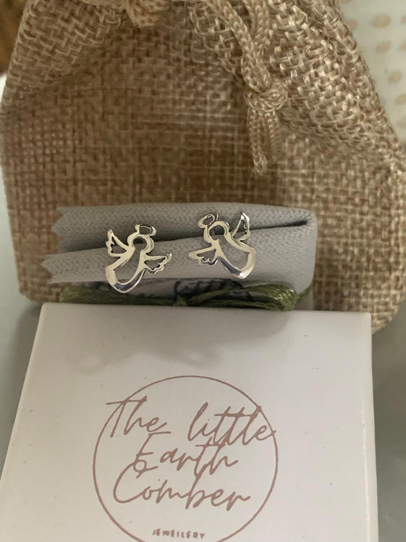 May include: A pair of silver angel earrings in a small white box with the text "The Little Earth Comber Jewellery" on the front.