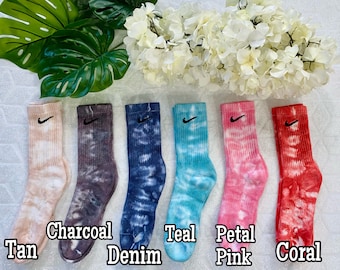 May include: Six pairs of tie-dye socks with a black Nike swoosh logo. The socks are in the colors tan, charcoal, denim, teal, petal pink, and coral.