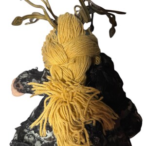 Pode incluir: Boneca artesanal com uma tran&ccedil;a de fio amarelo e um vestido de renda preto. O cabelo da boneca &eacute; uma tran&ccedil;a grossa de fio amarelo, e tem um adorno de cabe&ccedil;a decorativo. O vestido &eacute; preto com detalhes em renda.