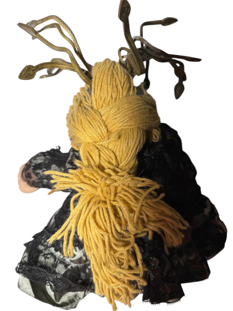 Pode incluir: Boneca artesanal com uma tran&ccedil;a de fio amarelo e um vestido de renda preto. O cabelo da boneca &eacute; uma tran&ccedil;a grossa de fio amarelo, e tem um adorno de cabe&ccedil;a decorativo. O vestido &eacute; preto com detalhes em renda.