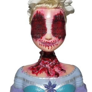 Pode incluir: Uma cabeça de boneca com um acessório de cabelo branco e cabelo loiro. Os olhos da boneca são cobertos com fio vermelho e a boca está costurada. A área do pescoço tem uma aparência sangrenta e sangrenta, e a boneca está colocada em uma base azul clara e roxa.