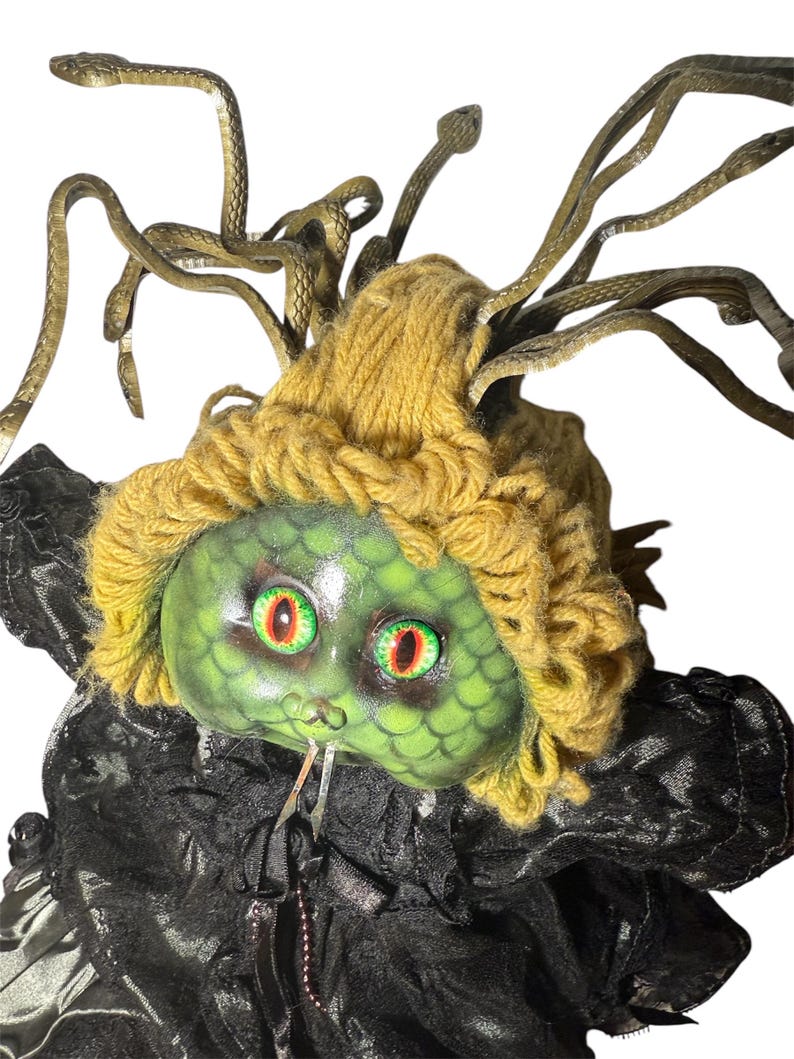 Pode incluir: Uma boneca Medusa com rosto verde, cabelo de fio amarelo e cabelo de cobra bronze. A boneca tem olhos vermelhos e verdes e usa uma roupa preta com babados. As cobras s&atilde;o posicionadas ao redor da cabe&ccedil;a.